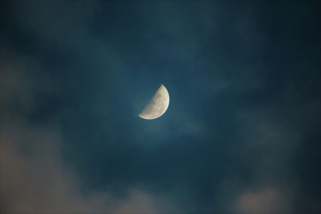 A serene view of the half moon surrounded by clouds in the night sky.